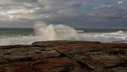 Stormy autumn afternoon with cold white spray from ocean waves crashing on basalt rocks