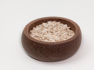 Raw oatmeal flakes in a rustic wooden bowl isolated on white