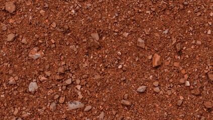 Detailed shot of coarse, reddish-brown earth with scattered small rocks and debris on a textured, dry, and possibly hardened surface.