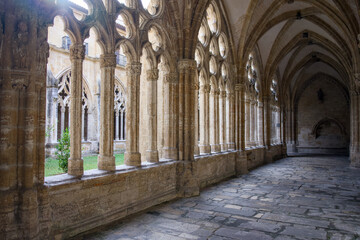 Historic gothic cloister corridor with repetitive stone arches columns and inner courtyard garden creating peaceful monastery atmosphere 