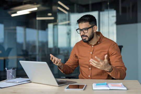 Male professional gesturing and explaining business concepts during a video call on laptop in a modern office, conducting a virtual meeting, training or presentation for remote team