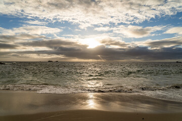 Coucher de soleil sur la mer d’Iroise, lumière dorée se reflétant sur le sable humide d’une...