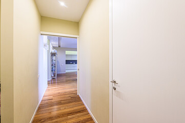 An interior view features a hallway with hardwood flooring and neutral-toned walls. A doorway leads to another room. A white door with silver hardware is visible on the right