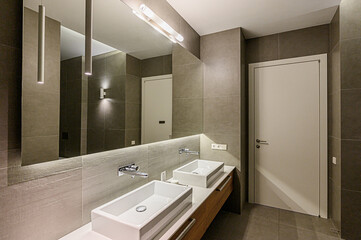 Modern bathroom features dual square sinks, large mirror, tile walls, and sleek lighting for a minimalist, clean aesthetic