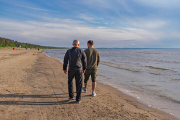 Rear view of father and son strolling along sandy shoreline, quiet conversation and generational bond in soft light
