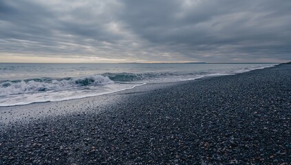 A rocky shoreline extends beside calm waters under an overcast sky at early morning, evoking peacefulness.