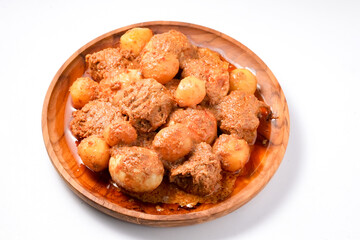 A top-down view of a wooden plate holding beef, hard-boiled eggs, and small potatoes cooked in a thick, brown Indonesian rendang sauce. Home cooking style