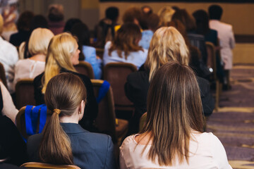 Female audience at the symposyum meeting, participants attendees in conference room hall listens to lecturer, group of women on a medical congress together listen to speaker on a stage at master-class