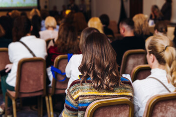 Female audience at the symposyum meeting, participants attendees in conference room hall listens to lecturer, group of women on a medical congress together listen to speaker on a stage at master-class