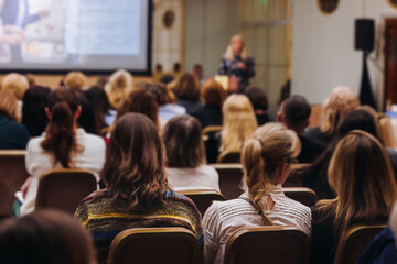 Female audience at the symposyum meeting, participants attendees in conference room hall listens to lecturer, group of women on a medical congress together listen to speaker on a stage at master-class