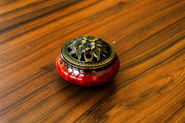 Elegant red ceramic incense burner with a detailed brass lid on a warm, polished wooden table. Perfect for relaxation, meditation, and decor
