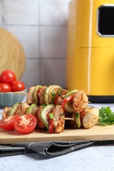 Tasty skewers with chicken, parsley, vegetables and air fryer on light grey table, closeup