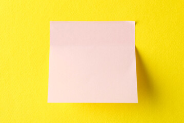 Blank pink note on yellow background, top view. Space for text