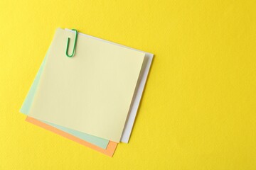 Blank colorful notes with paper clip on yellow background, top view. Space for text