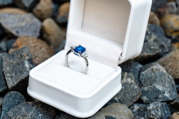 Stunning blue sapphire engagement ring in a white box, set against a backdrop of natural stones. Perfect for luxury and romance themes