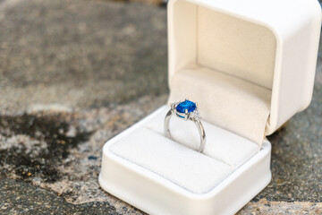 Stunning blue sapphire engagement ring in a white box, set against a backdrop of natural stones. Perfect for luxury and romance themes