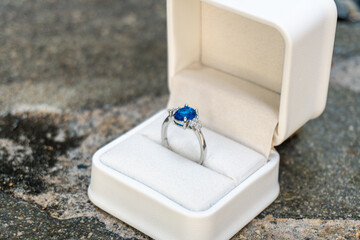 Stunning blue sapphire engagement ring in a white box, set against a backdrop of natural stones. Perfect for luxury and romance themes