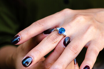 Close-up of a woman's hand wearing an elegant sapphire and diamond ring, with nails painted in a deep, rich burgundy color
