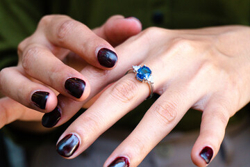 Close-up of a woman's hand wearing an elegant sapphire and diamond ring, with nails painted in a deep, rich burgundy color