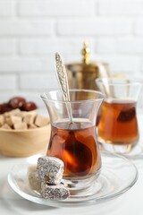 Tasty Turkish tea in glass cups, brown sugar and sweets on white table, closeup
