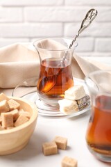 Tasty Turkish tea in glass cups, brown sugar and sweets on white marble table, closeup
