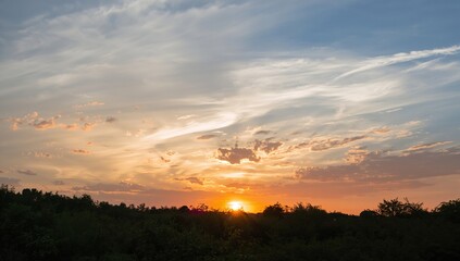 Fototapeta premium The sun sets as golden hues spread through the cloudy sky, illuminating the horizon.