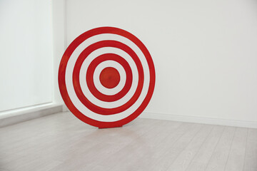 Round shooting target on floor near white wall indoors, space for text