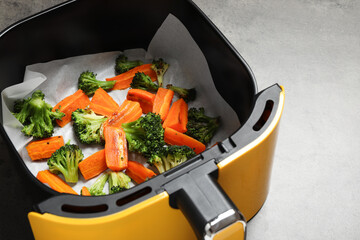 Grilled vegetables in air fryer basket on grey table, closeup