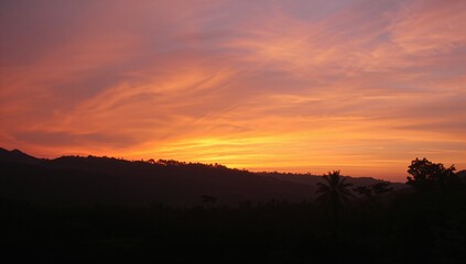 Sunrise scene featuring a vibrant orange and yellow sky gradient above a dark forest outline