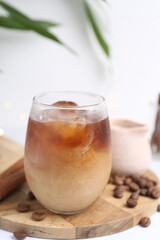 Tasty iced coffee in glass and beans on white table, closeup