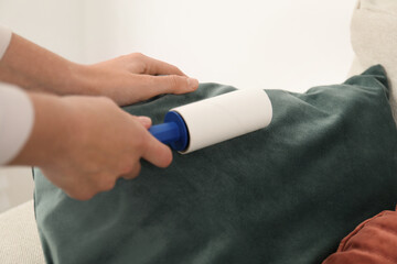 Woman cleaning cushion with lint roller at home, closeup