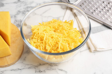 Grated cheese in bowl, fresh pieces and grater on white marble table, closeup