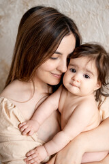 a mother with a baby, a young mom gently hugs and kisses her newborn baby, holding him in her arms, maternal love and care, a mother having fun with her child at home