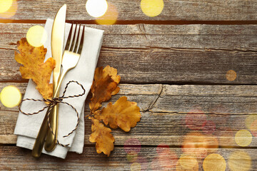 Autumn place setting with cutlery, napkin and golden leaves on wooden table, top view. Bokeh lights