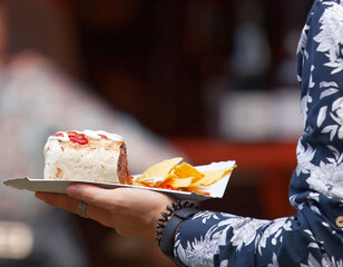 A person holding a paper tray with a burrito topped with sour cream and tomato salsa, served with tortilla chips at a street food market in Karlín, Prague.