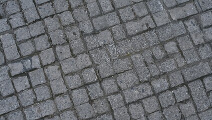 Zigzag layout of gray paving stones with a rough, moss-covered texture in a walkway