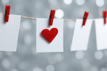 A white card with a red heart hangs on a clothesline with clothespins