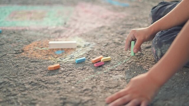 Green chalk in a child hand moves gently across the street. The drawing grows each new line, outdoor play fills the space with color and art. Chalk connects kid and child in happy street creativity.