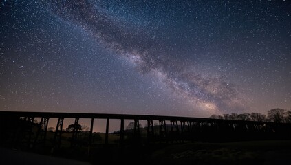 A railway bridge in the foreground beneath a star-filled night sky