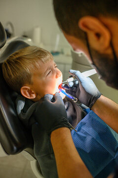 Little boy at dentist appointment sitting in chair while dentist uses dental drill and saliva ejector during treatment. Pediatric dentistry and oral care concept.