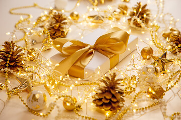 Luxury festive composition with white gift box and golden decorations on beige background. Christmas and New Year layout for greeting cards, invitations, or web banners.