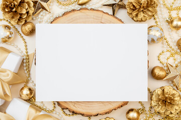 Horizontal blank sheet of paper on wooden slice surrounded by golden Christmas and New Year decorations. Flat lay with copy space for festive design or invitation.
