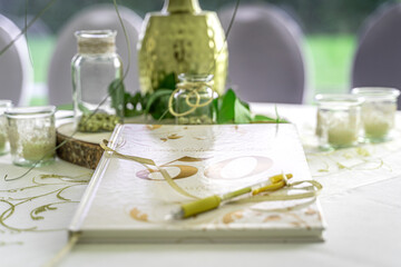 Eine Nahaufnahme eines Gästebuchs auf einem weißen Festtisch, festlich dekoriert für eine goldene Hochzeit. Das helle Buch mit dem Titel "Unsere Goldene Hochzeit" liegt mit einer goldenen Schleife und