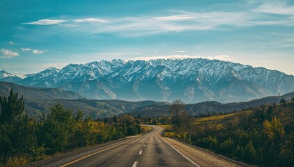 Fototapeta premium Beautiful highway leading to snowy peaks under a bright blue sky