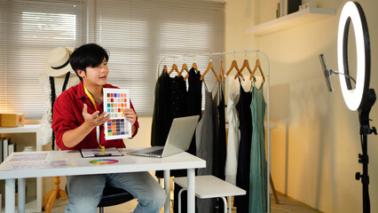 Portrait of young designer man stylish sitting and working.Attractive young man use laptop and colorful fabrics at fashion design studio