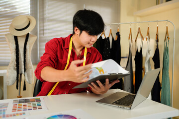 Male tailor work on items design with sketches, using laptop to review material and custom made sizes. Male professional tailor creating luxury clothes in workshop atelier