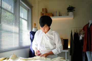 Young male tailor cutting fabric with scissors at table in dressmaking workshop.