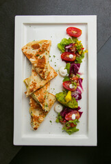A top-down view of a delicious-looking quesadilla with salad. The quesadilla is cut into triangles and plated on a rectangular plate with a side of colorful, fresh salad