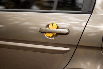 Yellow autumn leaf stuck in a car door handle, symbolizing fall season and nature meeting urban life.