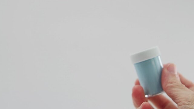 Mano che regge un flaconcino di tempera acrilica di colore azzurro chiaro su sfondo bianco